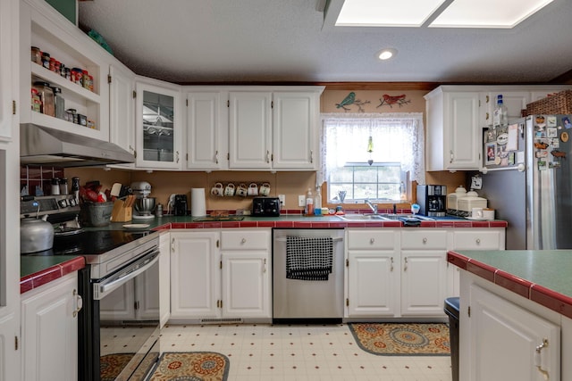 kitchen with appliances with stainless steel finishes, tile countertops, crown molding, and white cabinetry