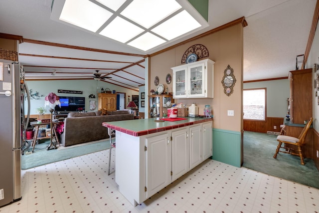 kitchen with white cabinets, vaulted ceiling with beams, ceiling fan, kitchen peninsula, and stainless steel fridge