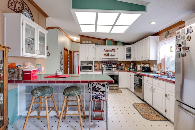 kitchen with stainless steel appliances, white cabinets, a kitchen bar, and kitchen peninsula