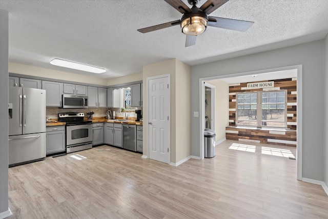 kitchen featuring gray cabinetry, stainless steel appliances, light hardwood / wood-style floors, ceiling fan, and tasteful backsplash