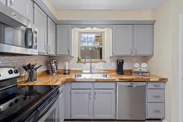 kitchen with tasteful backsplash, wood counters, sink, appliances with stainless steel finishes, and gray cabinetry