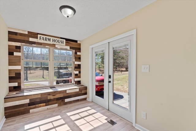 doorway with light wood-type flooring, french doors, a textured ceiling, and wood walls