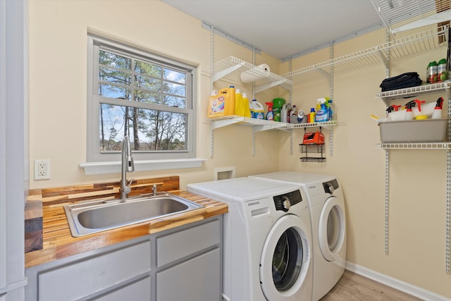 clothes washing area featuring light hardwood / wood-style floors, washing machine and clothes dryer, cabinets, and sink