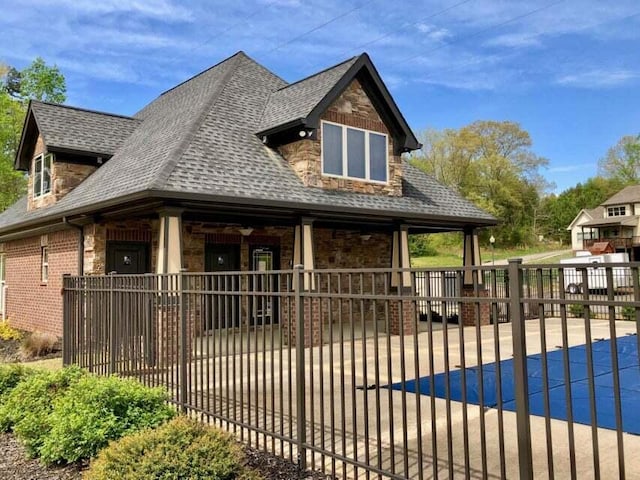 view of front facade with brick siding, a shingled roof, and fence