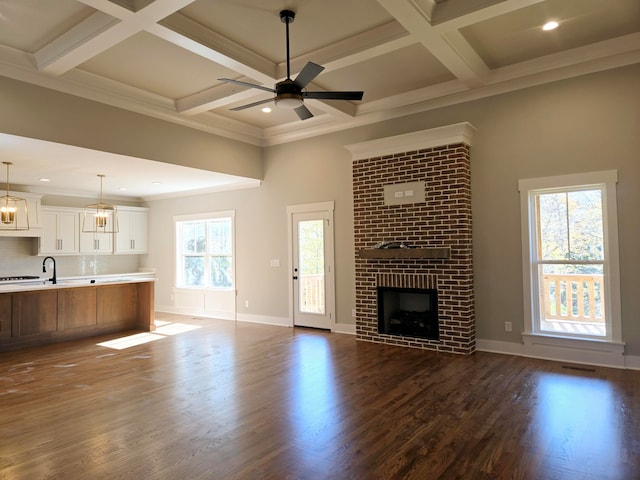 unfurnished living room with ceiling fan, dark wood-type flooring, coffered ceiling, a brick fireplace, and crown molding