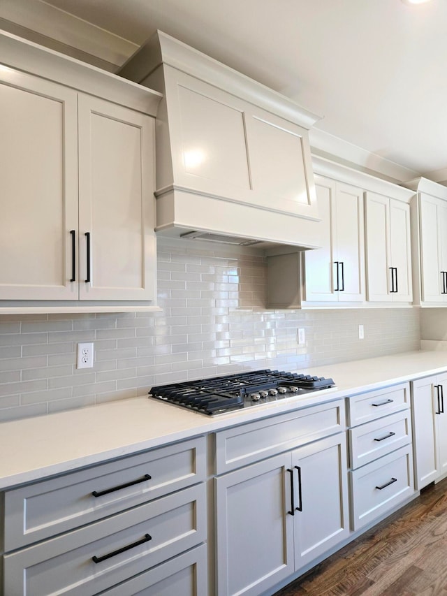 kitchen with decorative backsplash, premium range hood, stainless steel gas cooktop, dark wood-type flooring, and white cabinets