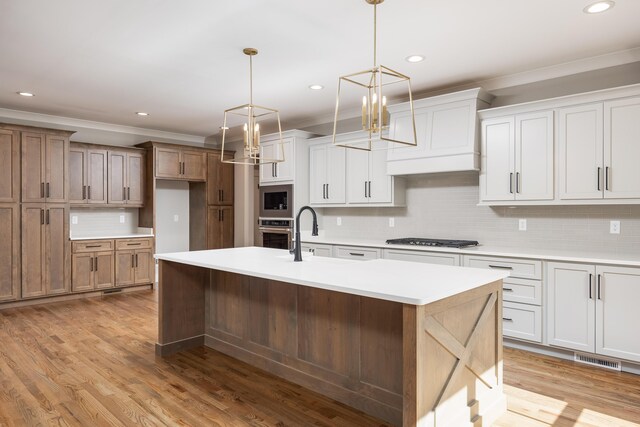 kitchen featuring light wood finished floors, stainless steel appliances, light countertops, and a kitchen island with sink