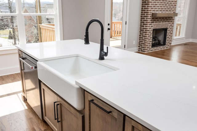 kitchen with a sink, a brick fireplace, dishwasher, and wood finished floors