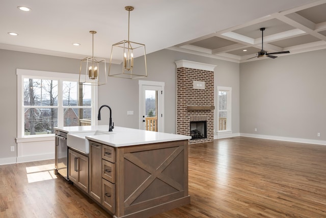 kitchen with wood finished floors, coffered ceiling, ceiling fan, a sink, and a brick fireplace