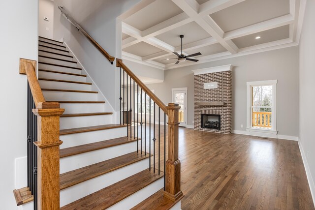 stairway with wood finished floors, baseboards, coffered ceiling, a fireplace, and ceiling fan