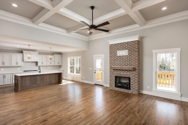 unfurnished living room with coffered ceiling, beam ceiling, a fireplace, and dark wood-type flooring