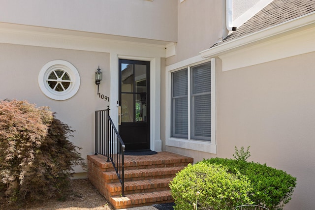 property entrance with stucco siding and a shingled roof