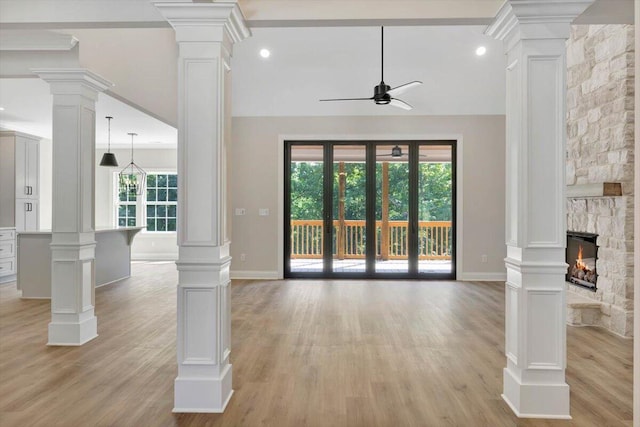 unfurnished living room with light hardwood / wood-style flooring, ceiling fan, a stone fireplace, and decorative columns