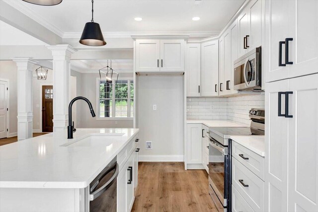 kitchen featuring a kitchen island with sink, light wood-type flooring, stainless steel appliances, decorative columns, and sink