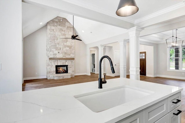 kitchen featuring a fireplace, ceiling fan with notable chandelier, dark hardwood / wood-style flooring, light stone countertops, and lofted ceiling with beams