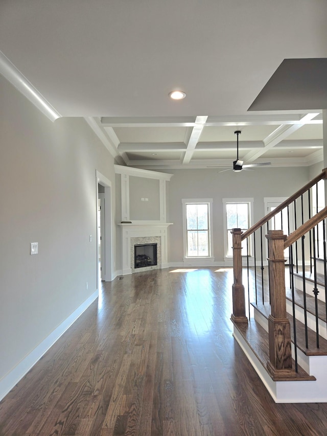 unfurnished living room featuring dark wood-style flooring, coffered ceiling, a fireplace, baseboards, and stairs