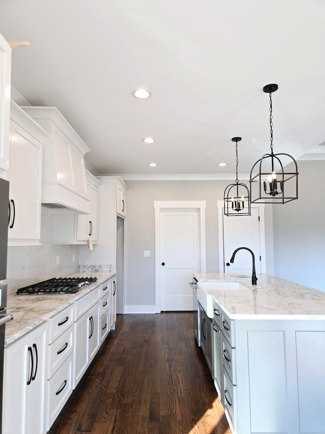 kitchen with stainless steel gas stovetop, light stone countertops, a center island with sink, and white cabinetry