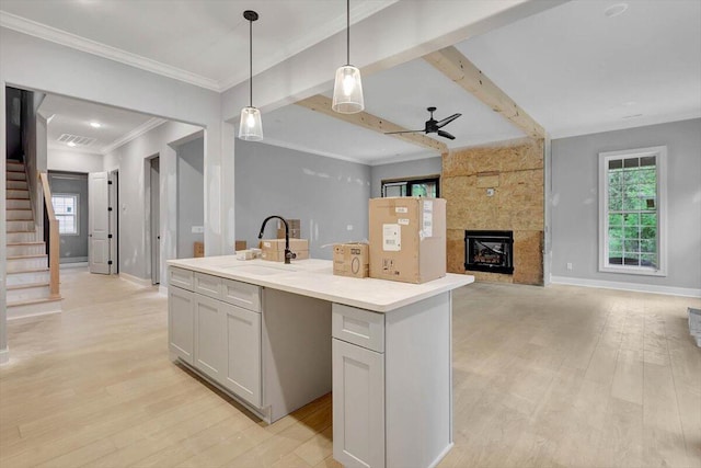 kitchen featuring ceiling fan, an island with sink, light wood-type flooring, decorative light fixtures, and a fireplace