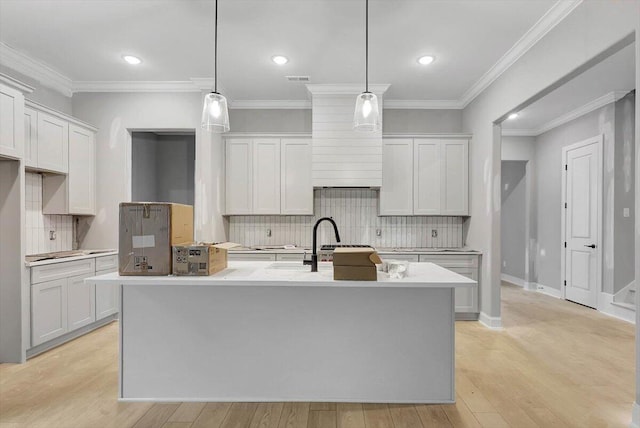 kitchen with light wood-type flooring, a center island with sink, white cabinetry, and decorative light fixtures