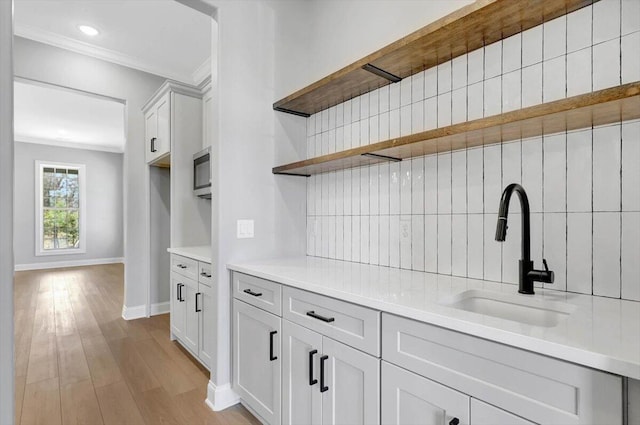 kitchen featuring sink, crown molding, light hardwood / wood-style flooring, white cabinetry, and tasteful backsplash