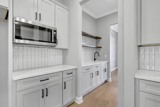 kitchen featuring tasteful backsplash, sink, ornamental molding, light hardwood / wood-style floors, and light stone countertops