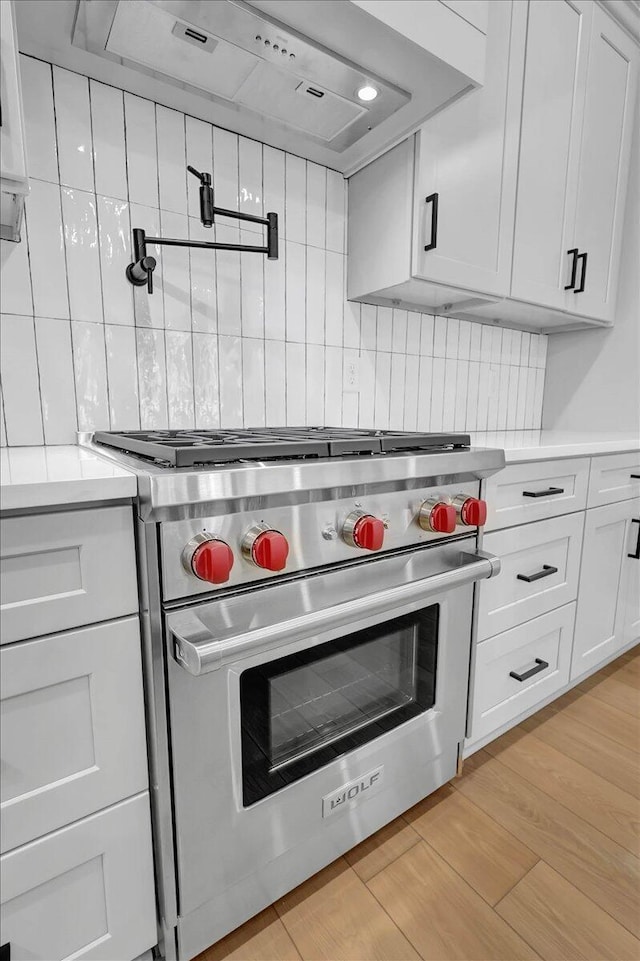 kitchen featuring light hardwood / wood-style flooring, white cabinetry, decorative backsplash, designer stove, and wall chimney exhaust hood