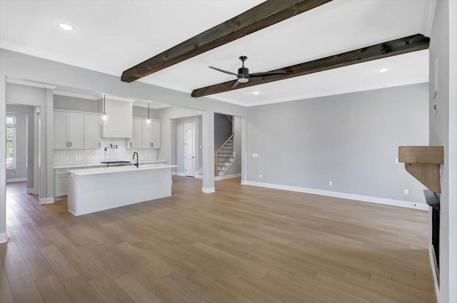 unfurnished living room featuring beam ceiling, ceiling fan, and light wood-type flooring