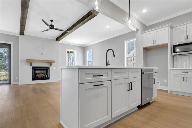 kitchen with appliances with stainless steel finishes, decorative light fixtures, beamed ceiling, white cabinets, and a center island with sink