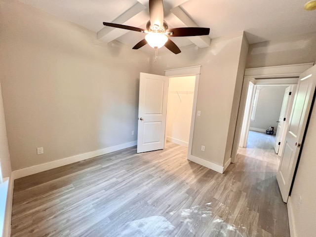 unfurnished bedroom with beam ceiling, ceiling fan, a walk in closet, a closet, and light wood-type flooring