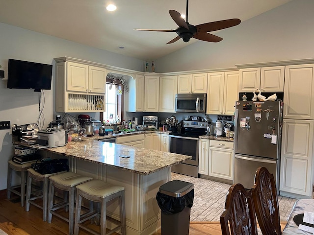 kitchen featuring stone countertops, vaulted ceiling, kitchen peninsula, ceiling fan, and appliances with stainless steel finishes