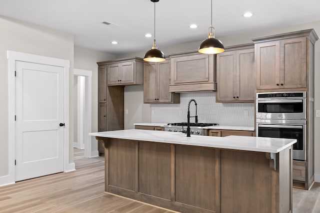 kitchen featuring tasteful backsplash, a kitchen island with sink, hanging light fixtures, and light hardwood / wood-style floors