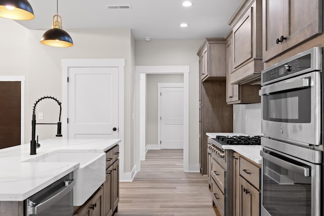 kitchen featuring light stone countertops, sink, stainless steel appliances, light hardwood / wood-style flooring, and pendant lighting