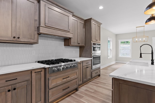 kitchen with light stone countertops, stainless steel appliances, sink, pendant lighting, and light hardwood / wood-style flooring