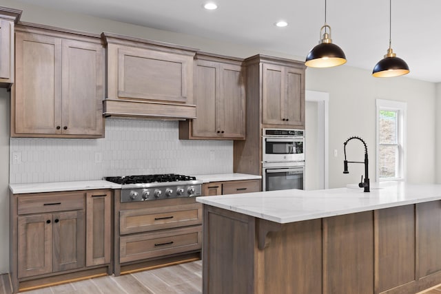 kitchen with tasteful backsplash, light stone counters, light hardwood / wood-style flooring, pendant lighting, and appliances with stainless steel finishes