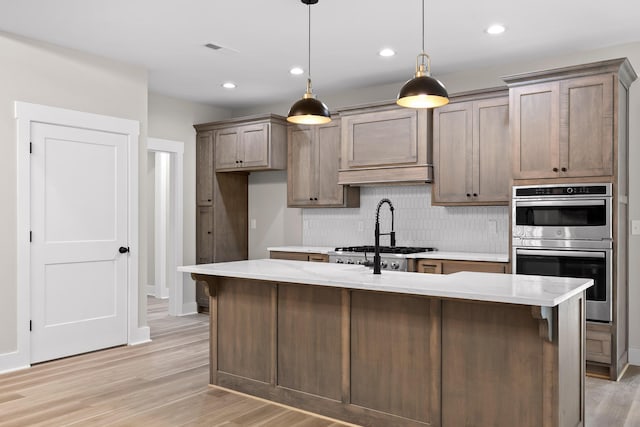 kitchen featuring pendant lighting, decorative backsplash, light wood-type flooring, and an island with sink