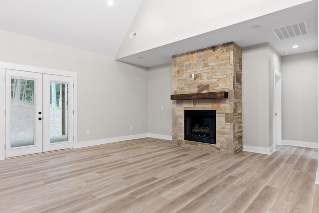 unfurnished living room featuring a stone fireplace, light wood-type flooring, high vaulted ceiling, and french doors