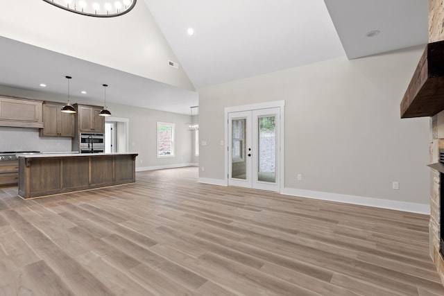 unfurnished living room with french doors, light hardwood / wood-style floors, high vaulted ceiling, and a notable chandelier