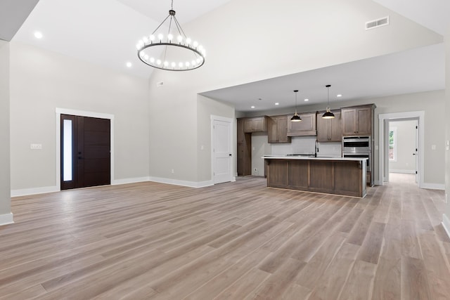 kitchen featuring light wood-type flooring, stainless steel double oven, pendant lighting, a center island with sink, and an inviting chandelier