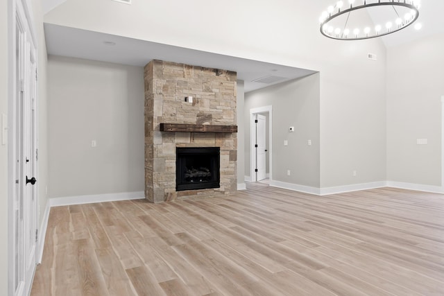 unfurnished living room with a stone fireplace, an inviting chandelier, and light wood-type flooring