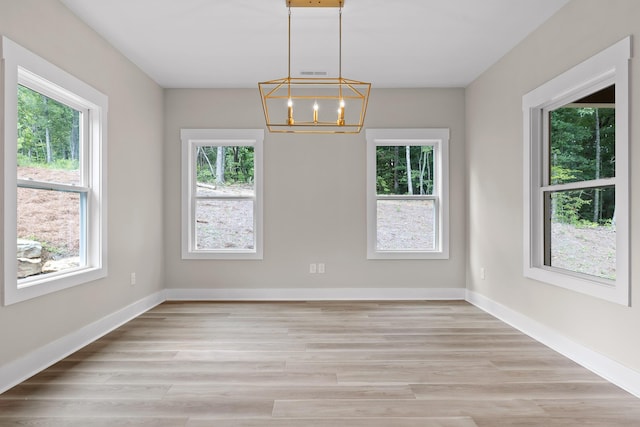 spare room featuring a notable chandelier, a healthy amount of sunlight, and light hardwood / wood-style flooring