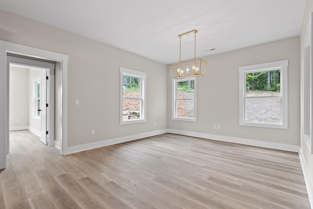 spare room featuring light hardwood / wood-style floors, an inviting chandelier, and a wealth of natural light