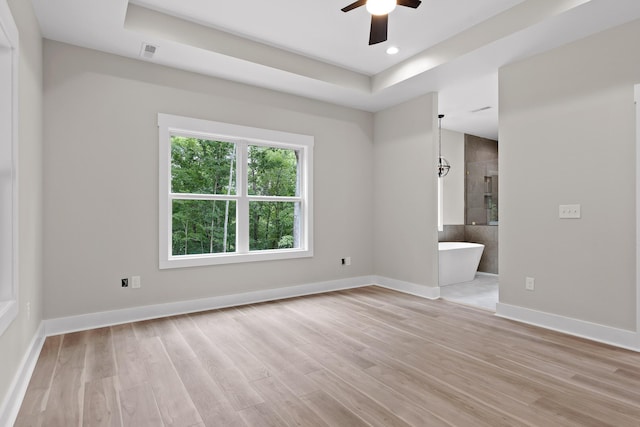 empty room featuring ceiling fan, light wood-type flooring, and a tray ceiling