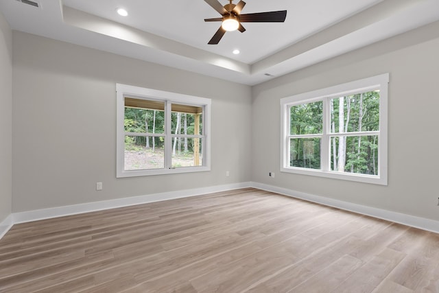 spare room featuring a tray ceiling, plenty of natural light, light hardwood / wood-style floors, and ceiling fan