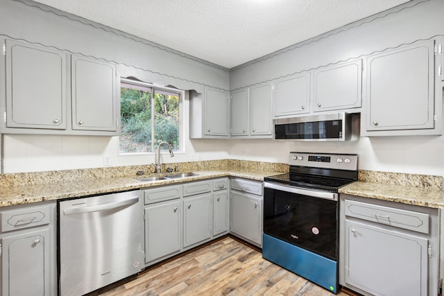 kitchen with stainless steel appliances, light hardwood / wood-style floors, a textured ceiling, and sink