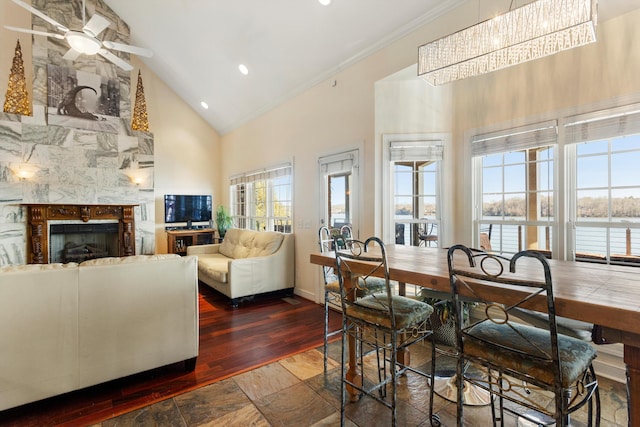 dining area featuring a tile fireplace, ceiling fan, crown molding, and high vaulted ceiling