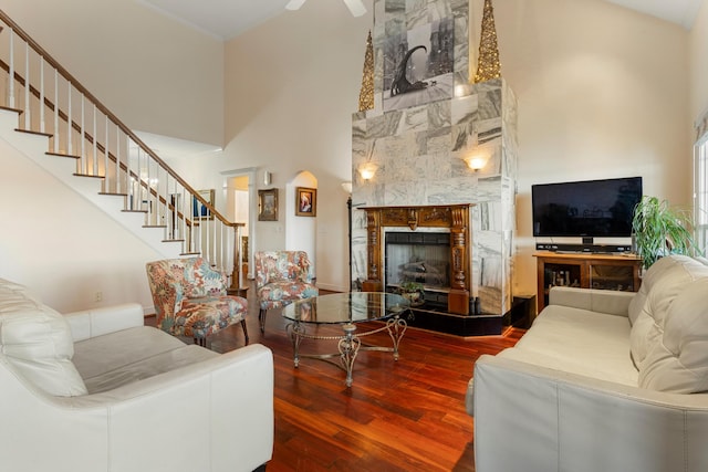 living room with a stone fireplace, ceiling fan, hardwood / wood-style floors, and a towering ceiling