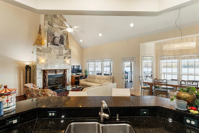 kitchen with ceiling fan, sink, a stone fireplace, dark stone countertops, and ornamental molding