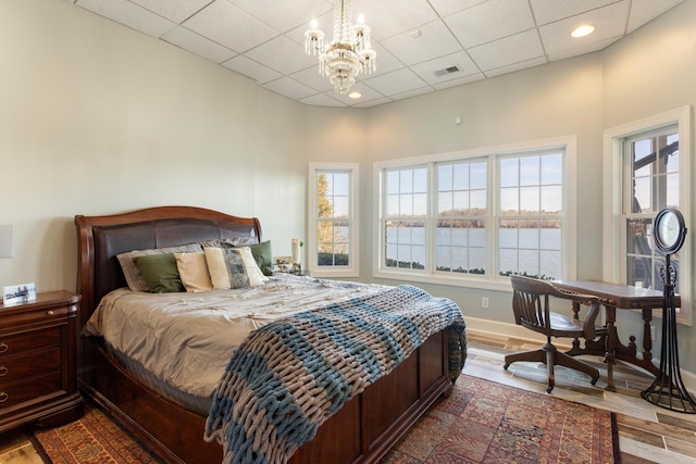 bedroom featuring hardwood / wood-style floors, a paneled ceiling, a water view, and a notable chandelier