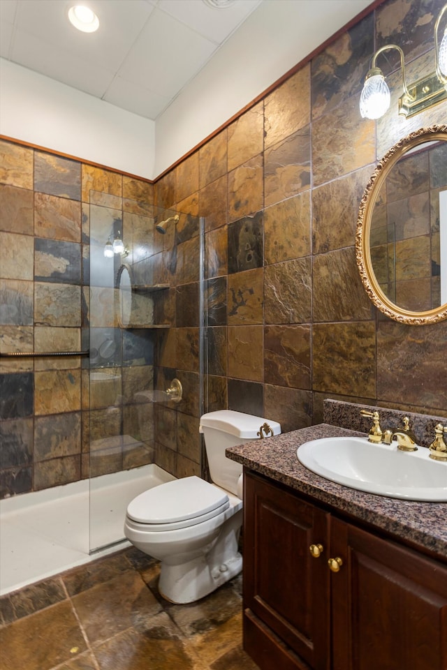 bathroom with a shower, vanity, tile walls, and toilet