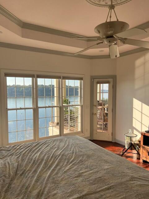 unfurnished bedroom with ceiling fan, a water view, wood-type flooring, and crown molding